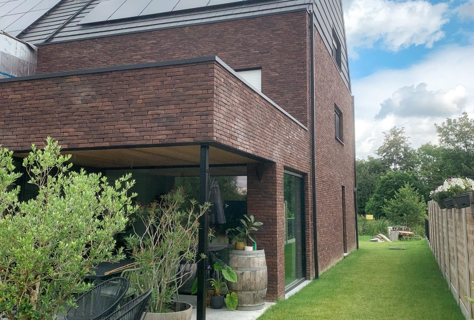 Afgewerkte nieuwbouw eengezinswoning in houtskelet met bakstenen gevelbekleding, overdekt terras en zonnepanelen op hellend dak in Drongen